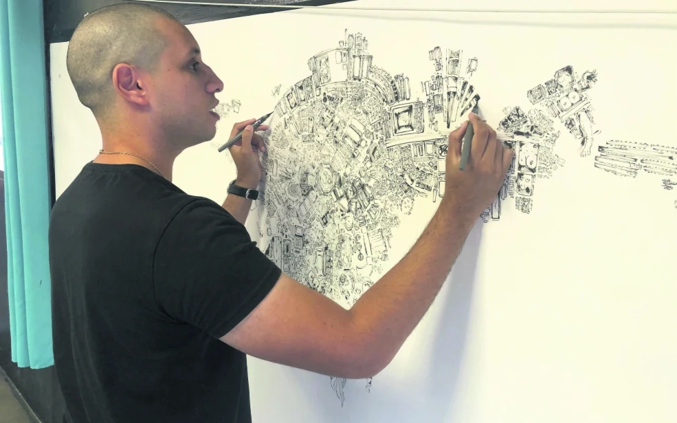 Isia dessine une composition panoramique à l’encre de Chine sur une grande feuille.