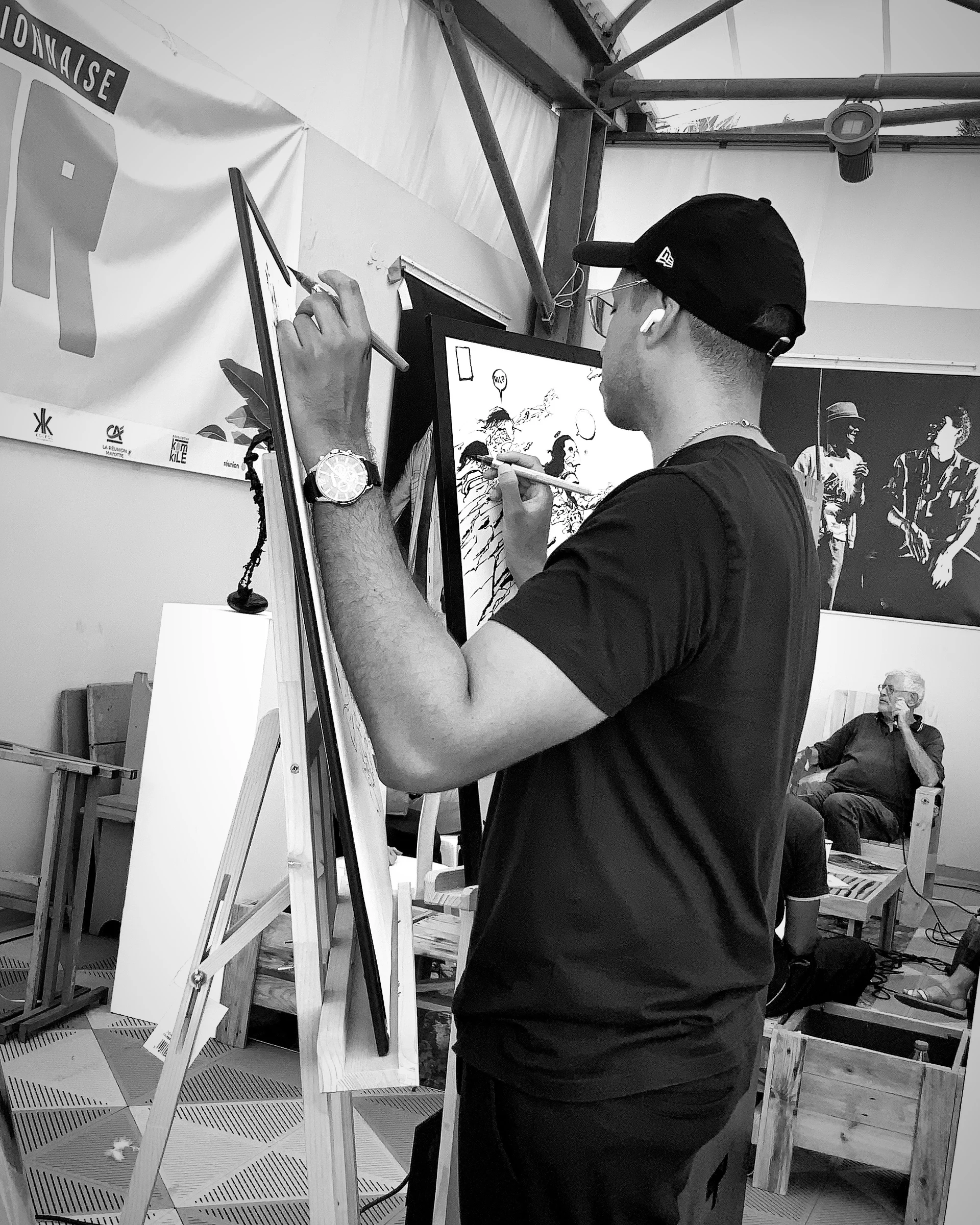 Isia dessine en direct sur un chevalet lors d’une performance en noir et blanc.